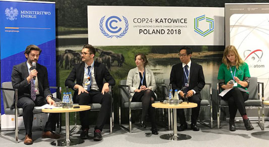 three men (one with a microphone) and two women seated in front of three banners, including a COP 24 banner